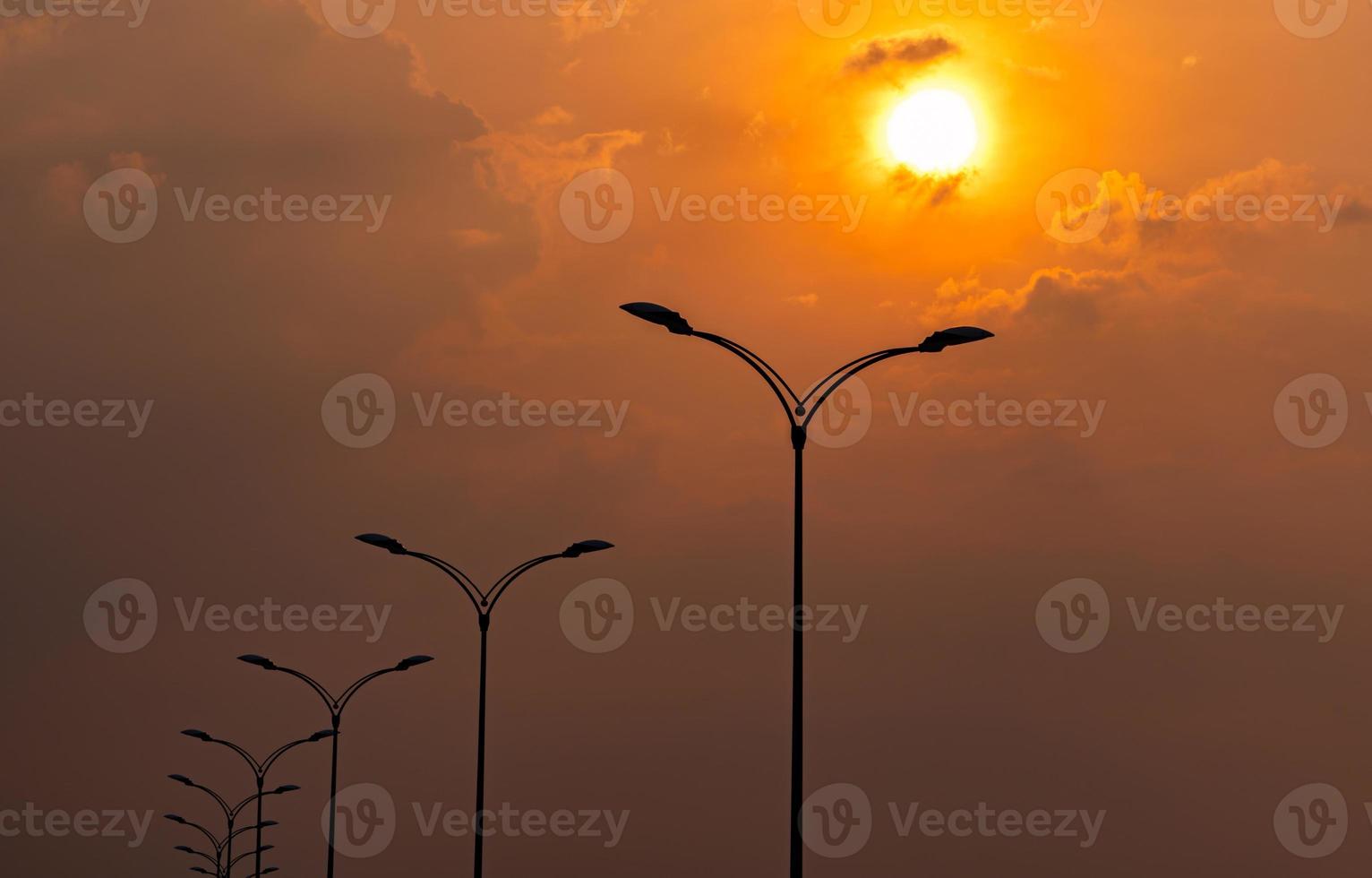 siluett gatan elektrisk stolpe med vacker orange och gul solnedgång himmel och moln på kvällen. gatlykta ljus. city road lyktstolpe för belysningskraft och energisparkoncept. foto