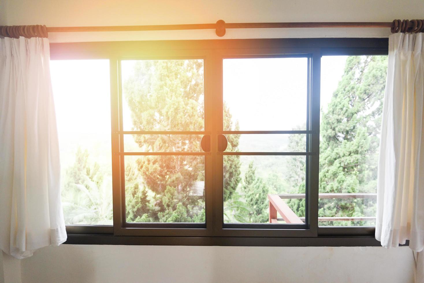 sovrumsfönster på morgonen - solljus genom i rummet öppna gardiner med balkong och naturträd på utanför fönstret foto
