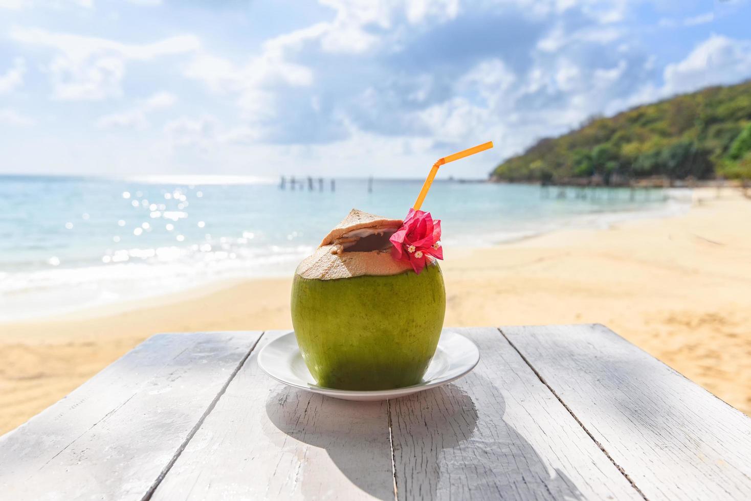 kokosnöt tropisk frukt på bord och sandstrand bakgrund vatten - färsk kokosjuice sommar med blomma på stranden hav i varmt väder hav landskap natur utomhus semester, ung kokosnöt foto