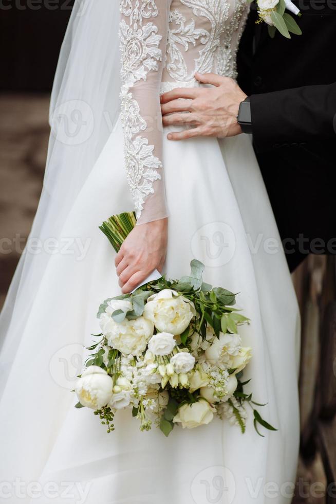 bruden i en elegant bröllopsklänning håller en vacker bukett med olika blommor och gröna blad. bröllopstema foto