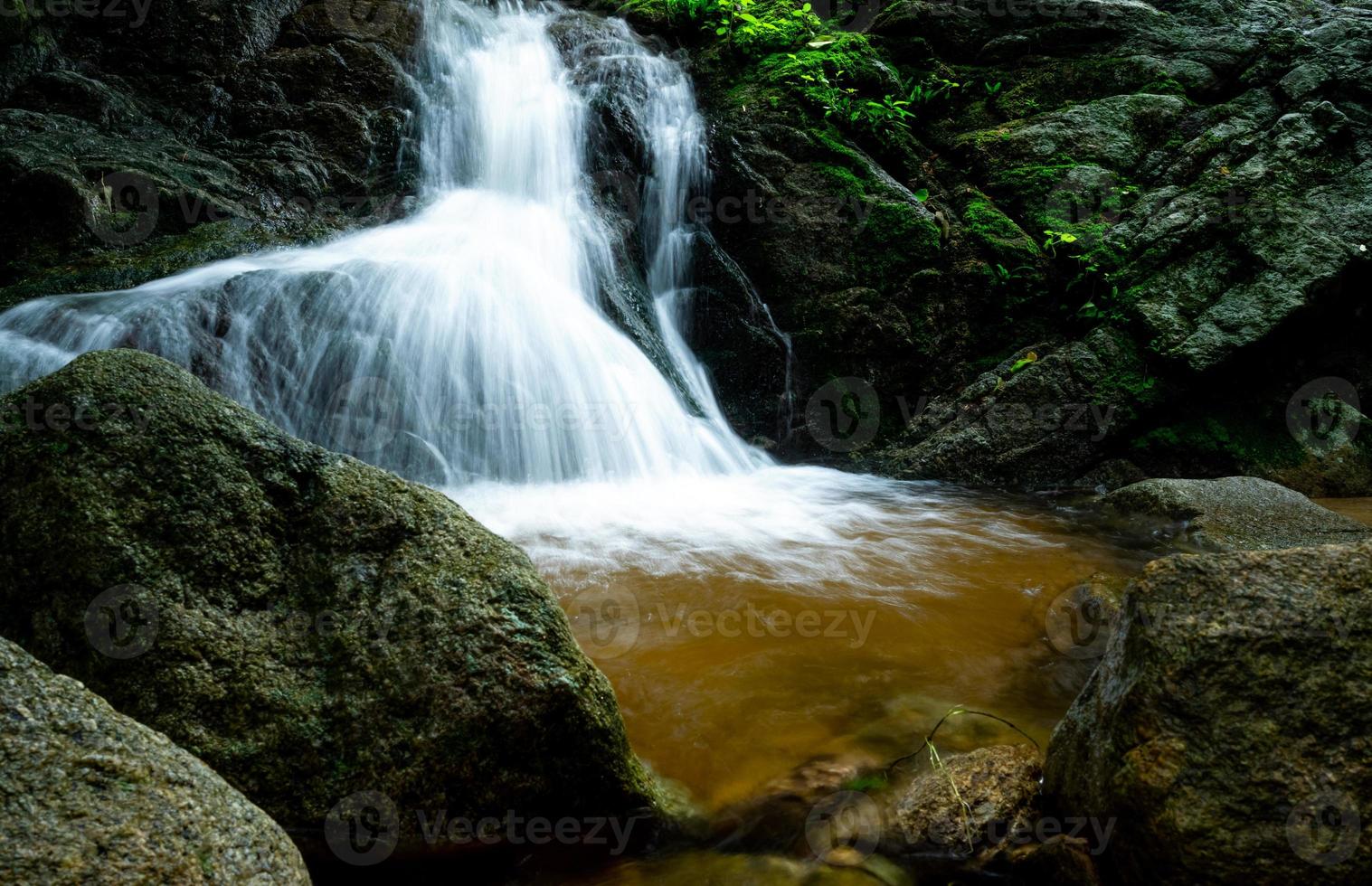 vackert vattenfall i djungeln. vattenfall i tropisk skog med grönt träd och solljus. vattenfallet rinner i djungeln. natur bakgrund. sten eller sten vid vattenfallet. fotografering med lång exponering. foto