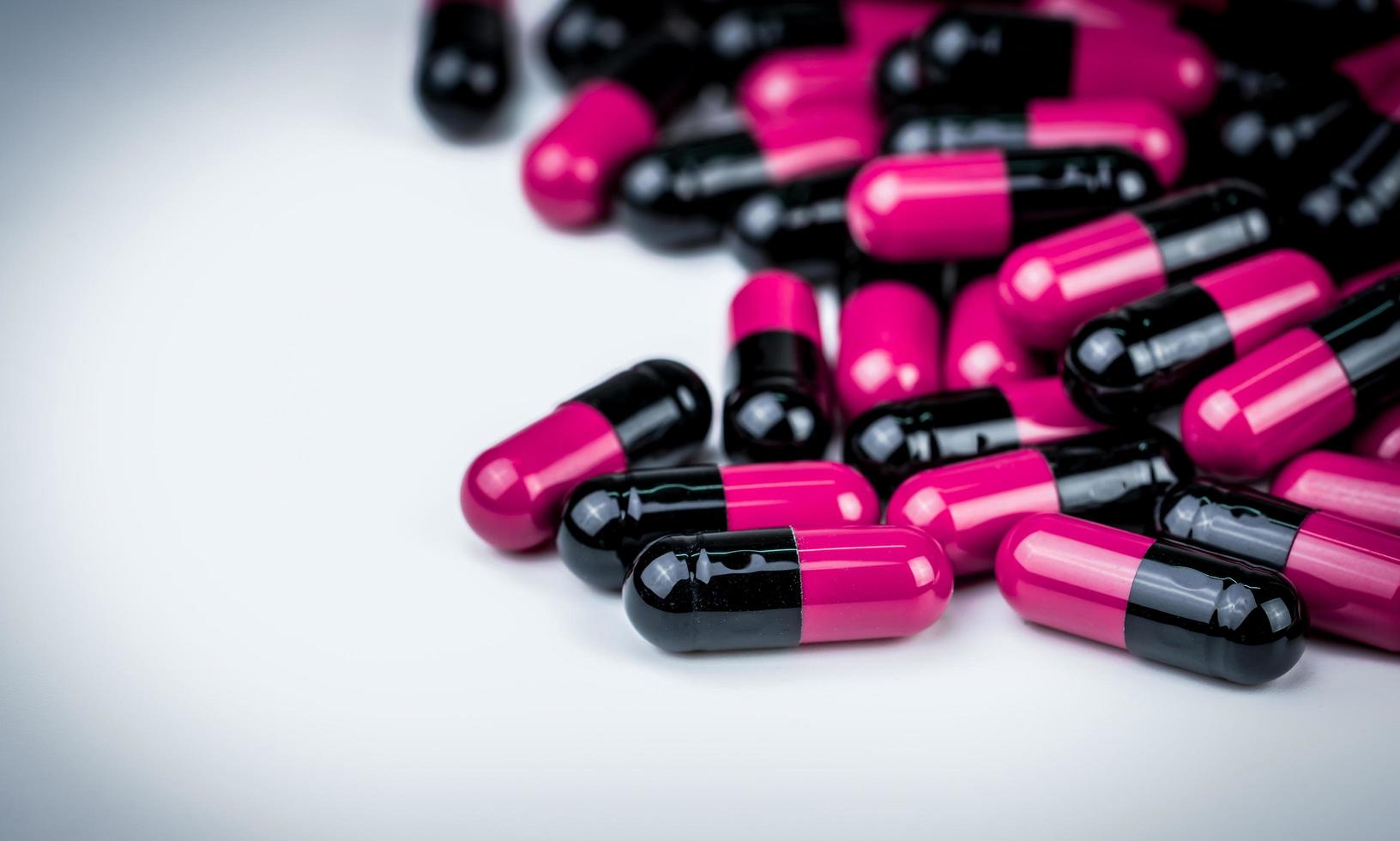 rosa-svart kapsel piller på vitt bord. antibiotikaresistens. global sjukvård. antimikrobiella kapselpiller. apotek bakgrund. antibiotikadroganvändning med rimliga. läkemedelsindustri. foto