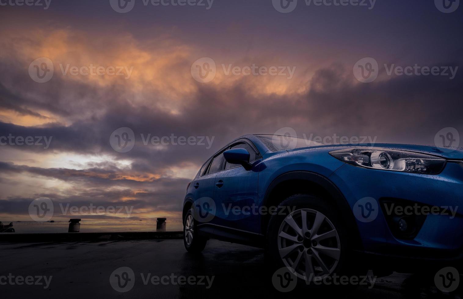 lyxsuvbil med regndroppar. framifrån ny blå suv bil parkerad på betong parkeringsplats nära havet strand med solnedgång himlen. elfordon koncept. bilresa. bil täckt med vattendroppar. foto