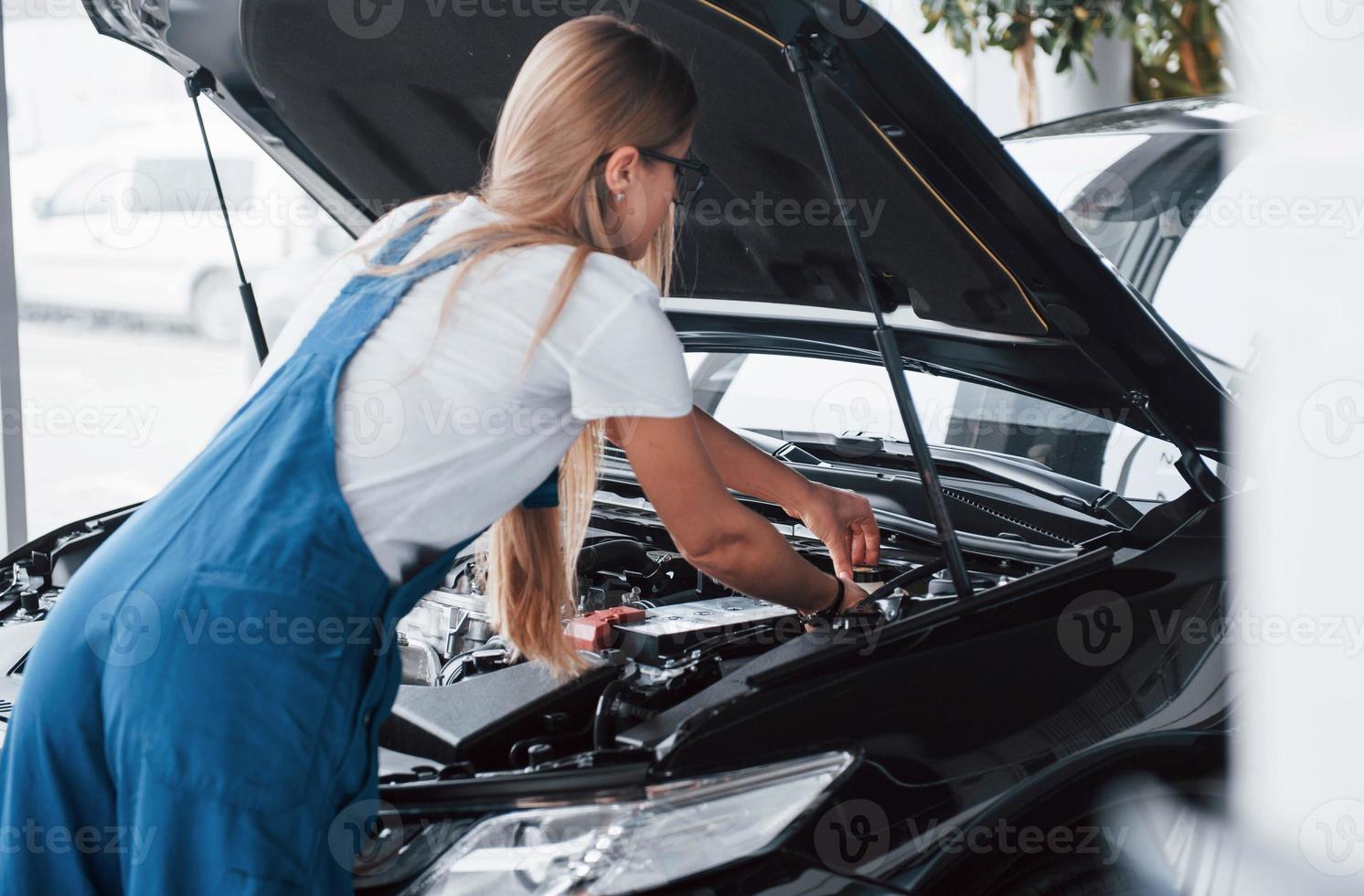 gör hårt arbete. på det fina jobbet. bilberoende kvinna reparerar svart bil inomhus foto