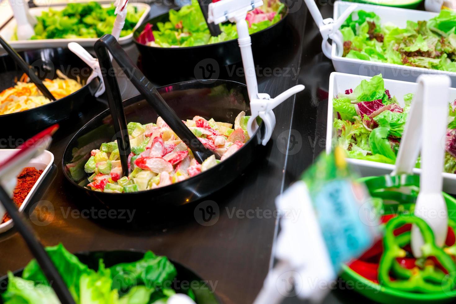 salladsbar buffé på restaurang. fräsch salladsbarbuffé till lunch eller middag. hälsosam mat. färsk grön och lila sallad i vit platta. selleri och krabba sticka skivad i svart skål. vegetarisk mat. foto