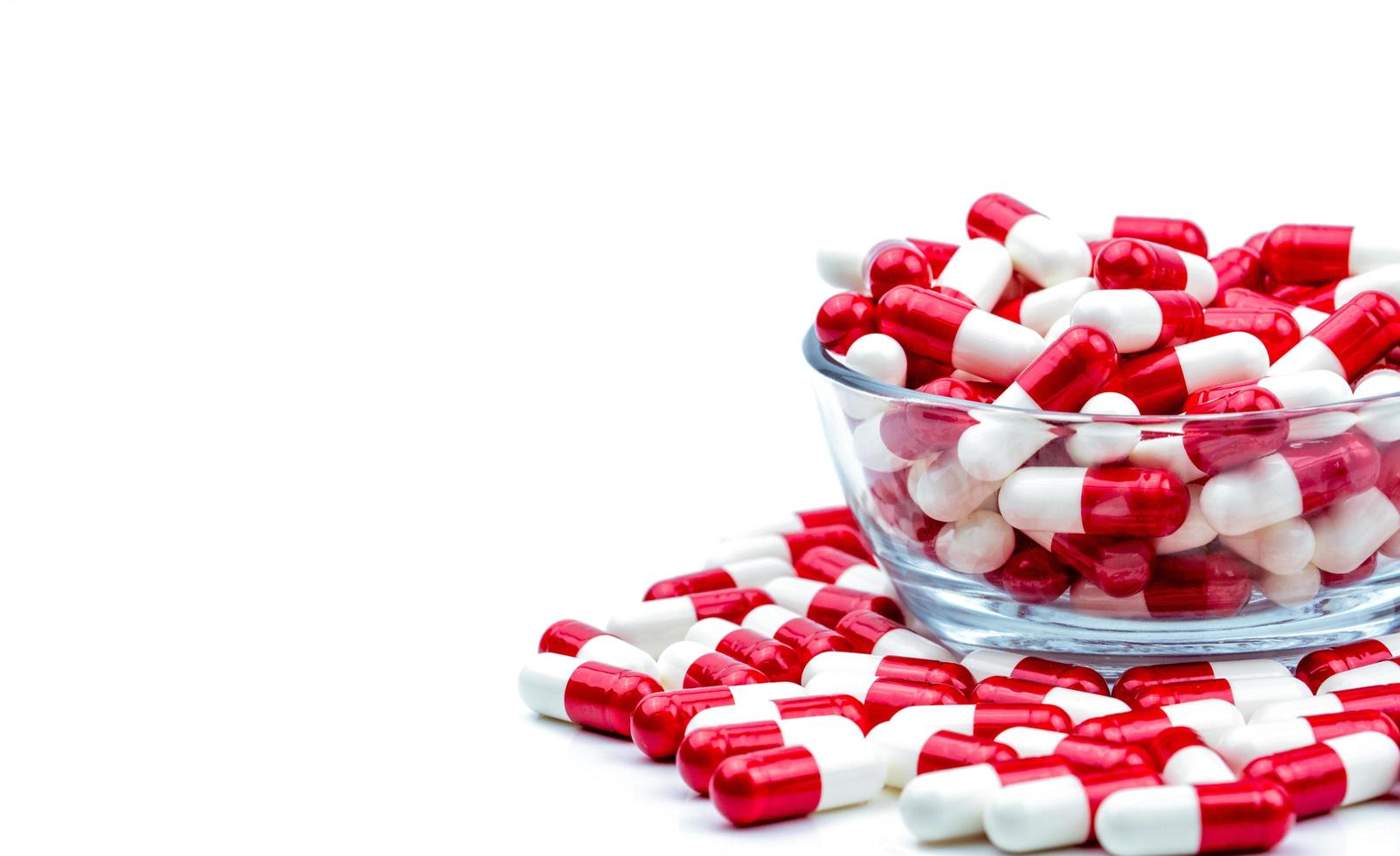 röda, vita antibiotikakapslar piller i glasskål och några på vit bakgrund med kopia utrymme. läkemedelsresistens koncept. antibiotikadroganvändning med rimligt och globalt hälsokoncept. foto