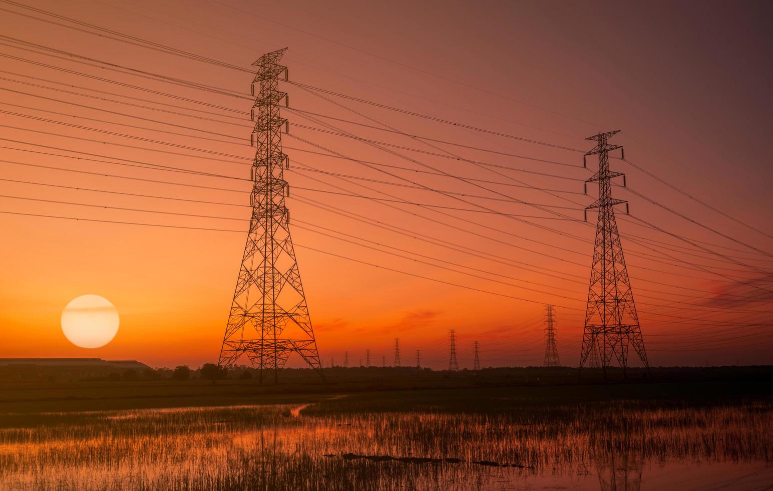 hög spänning elektrisk pylon och elektrisk ledning med solnedgång himlen. elstolpar. kraft och energi koncept. högspänningsnättorn med trådkabel. vacker stor sol vid solnedgången med röd-orange himmel. foto