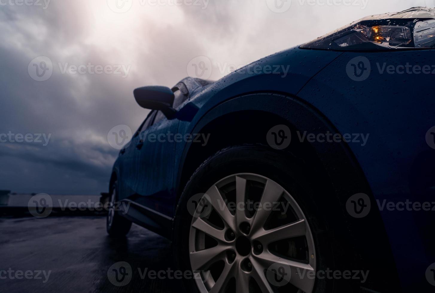 ny lyxig blå suv-bil parkerad på betongväg bredvid stranden en regnig dag med stormig himmel. framifrån av blå suv bil med sport design. regndroppar på bilen. bilresa. körning i dåligt väder. foto