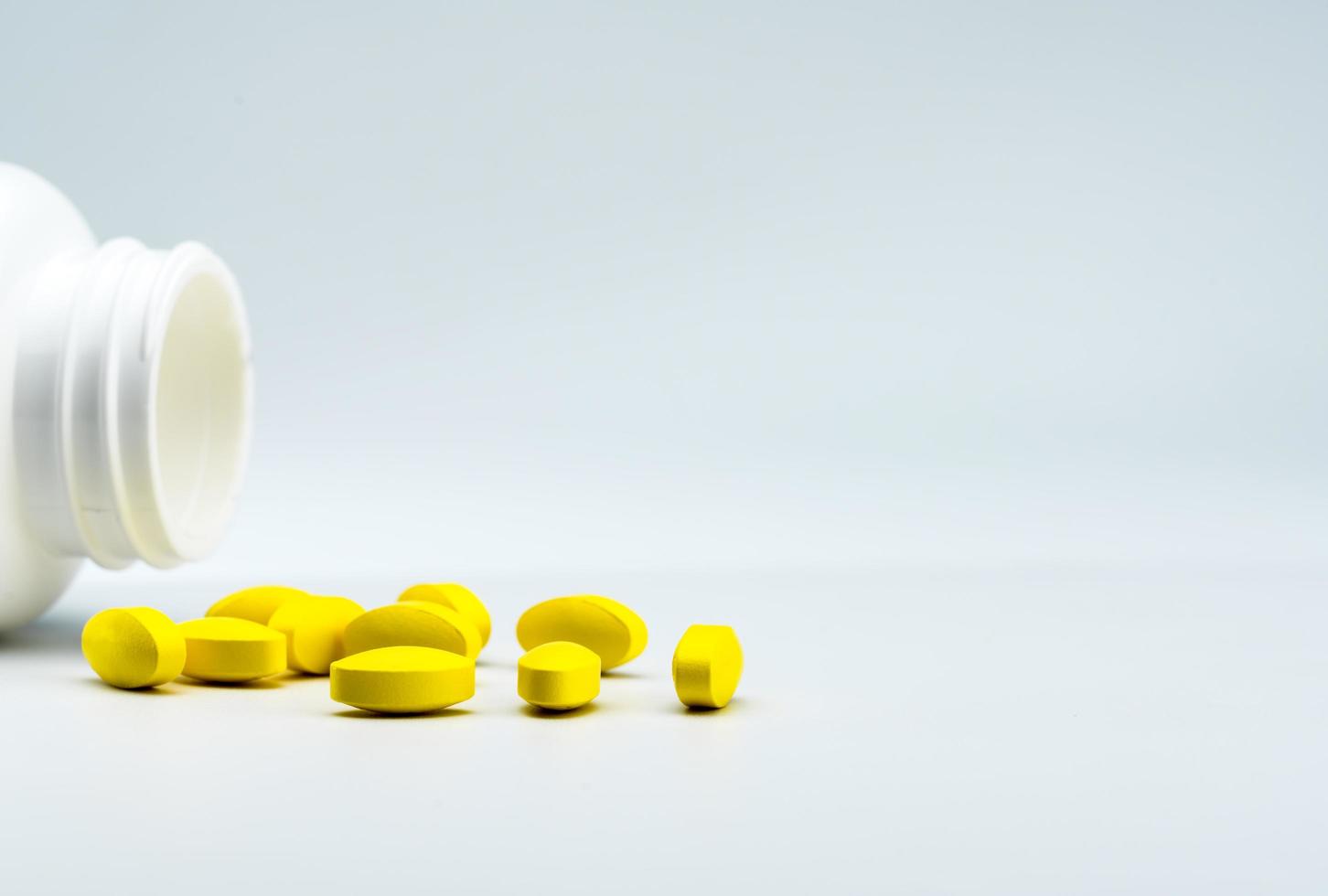 gula ovala tablettpiller och öppnad vit flaska på vit bakgrund med vackra kreativa mönster och kopieringsutrymme för text. mild till måttlig smärtbehandling. smärtstillande medicin. foto