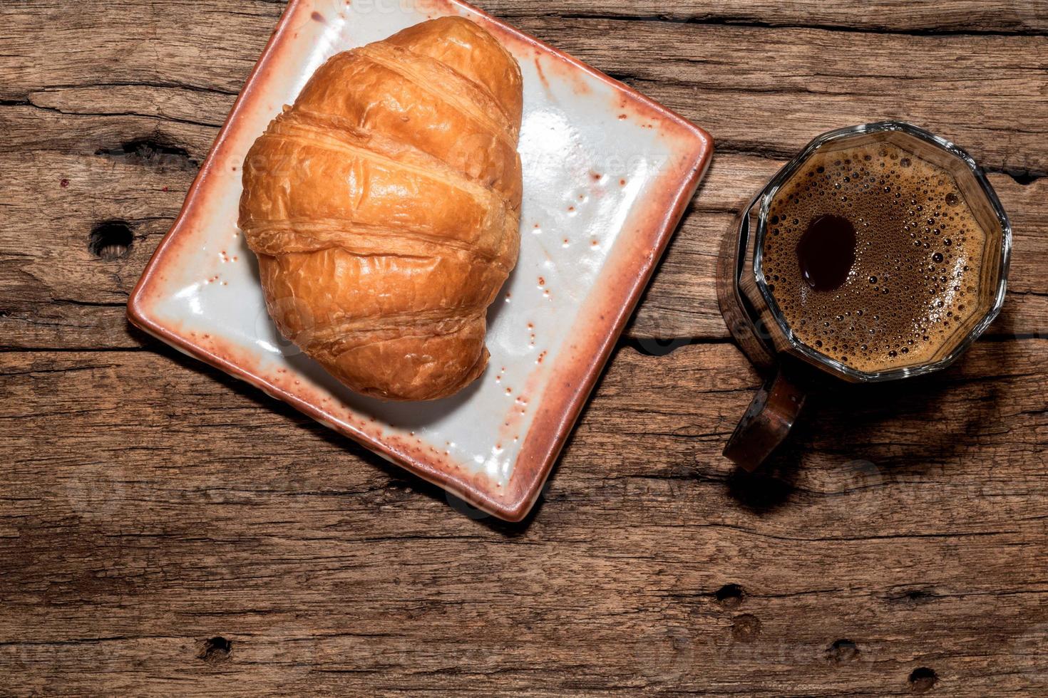 frukostmat croissant i tallrik och kaffe på träbord. foto