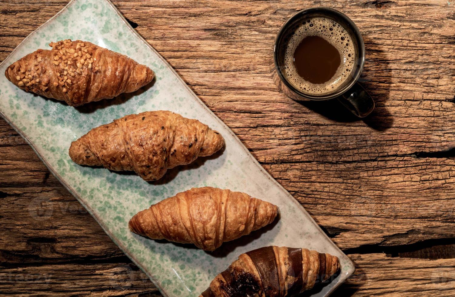 frukostmat croissant i tallrik och kaffe på träbord. foto