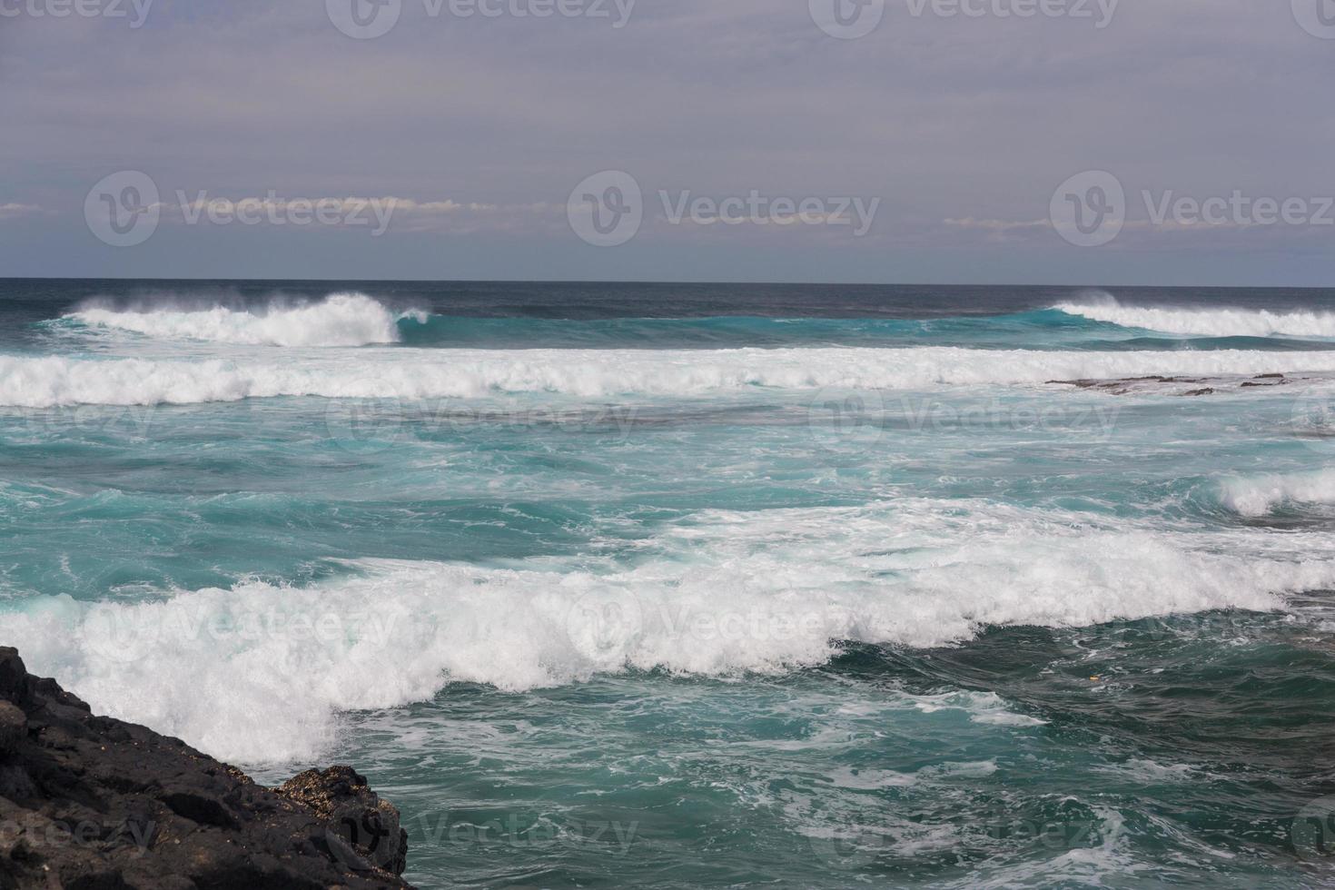 turbulenta havsvågor med vitt skum slår kuststenar foto