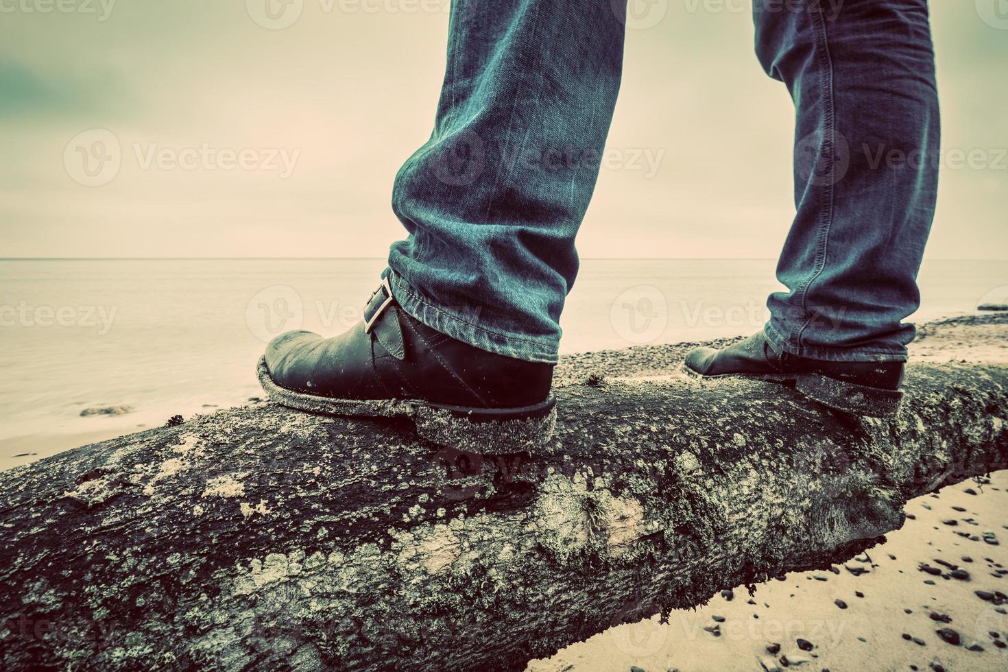 man i jeans och eleganta skor står på fallna träd på vilda stranden tittar på havet. årgång foto