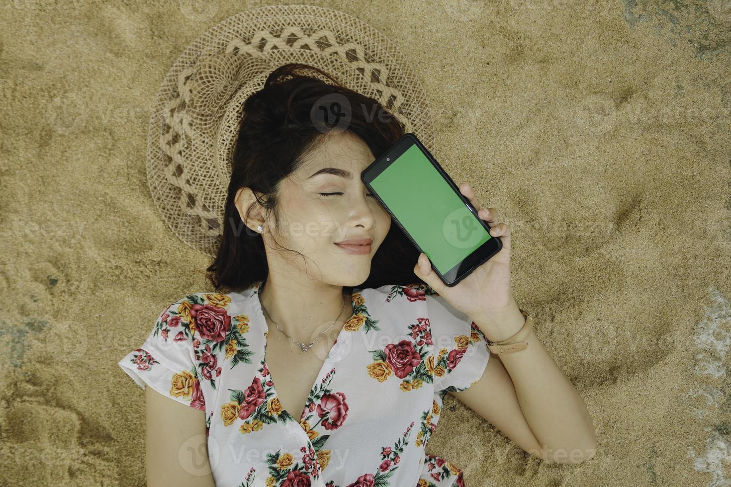 en ung vacker asiatisk kvinna som ligger på sanden medan hon visar telefonens skärm foto