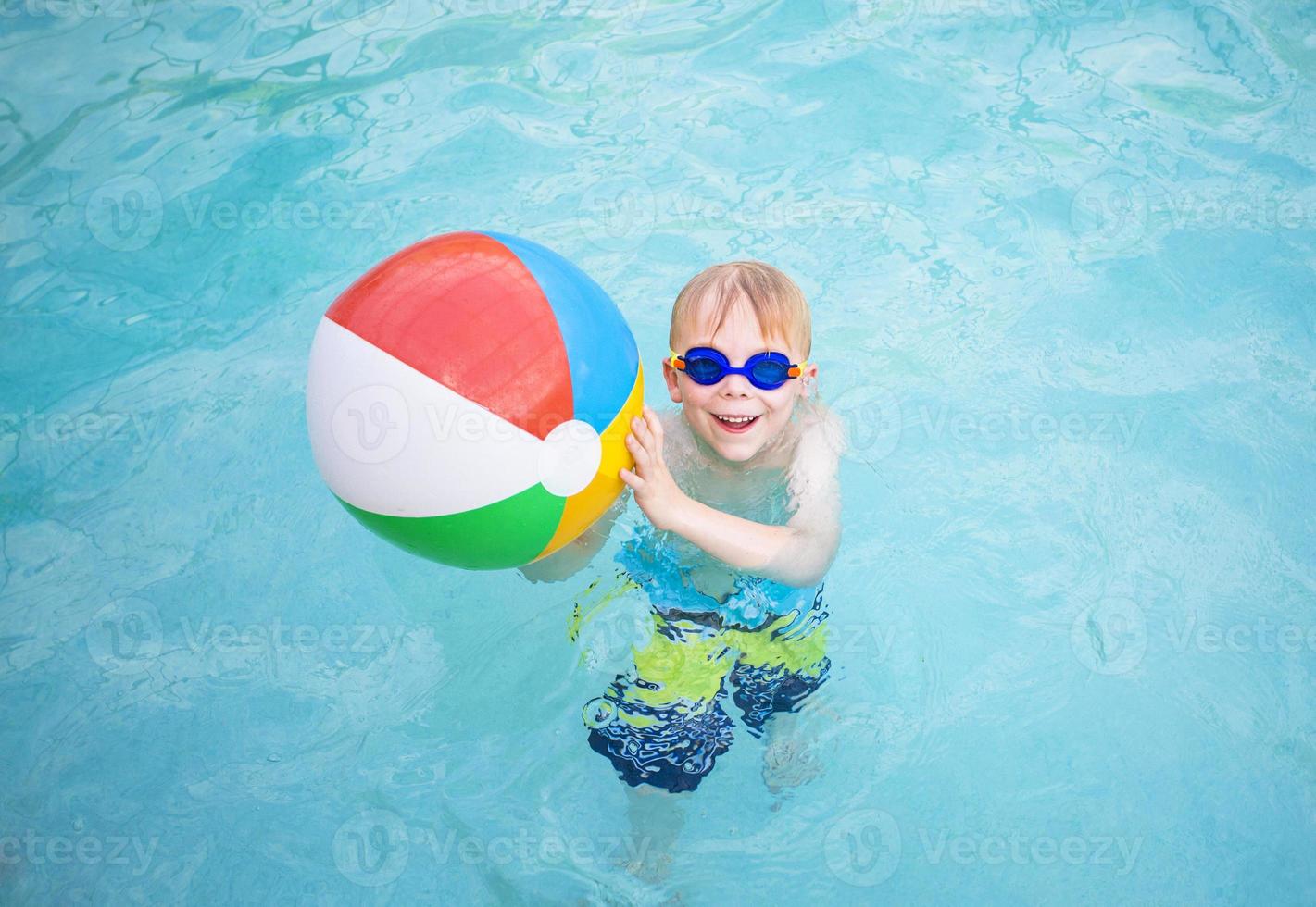 söt liten pojke som leker med strandboll i poolen foto