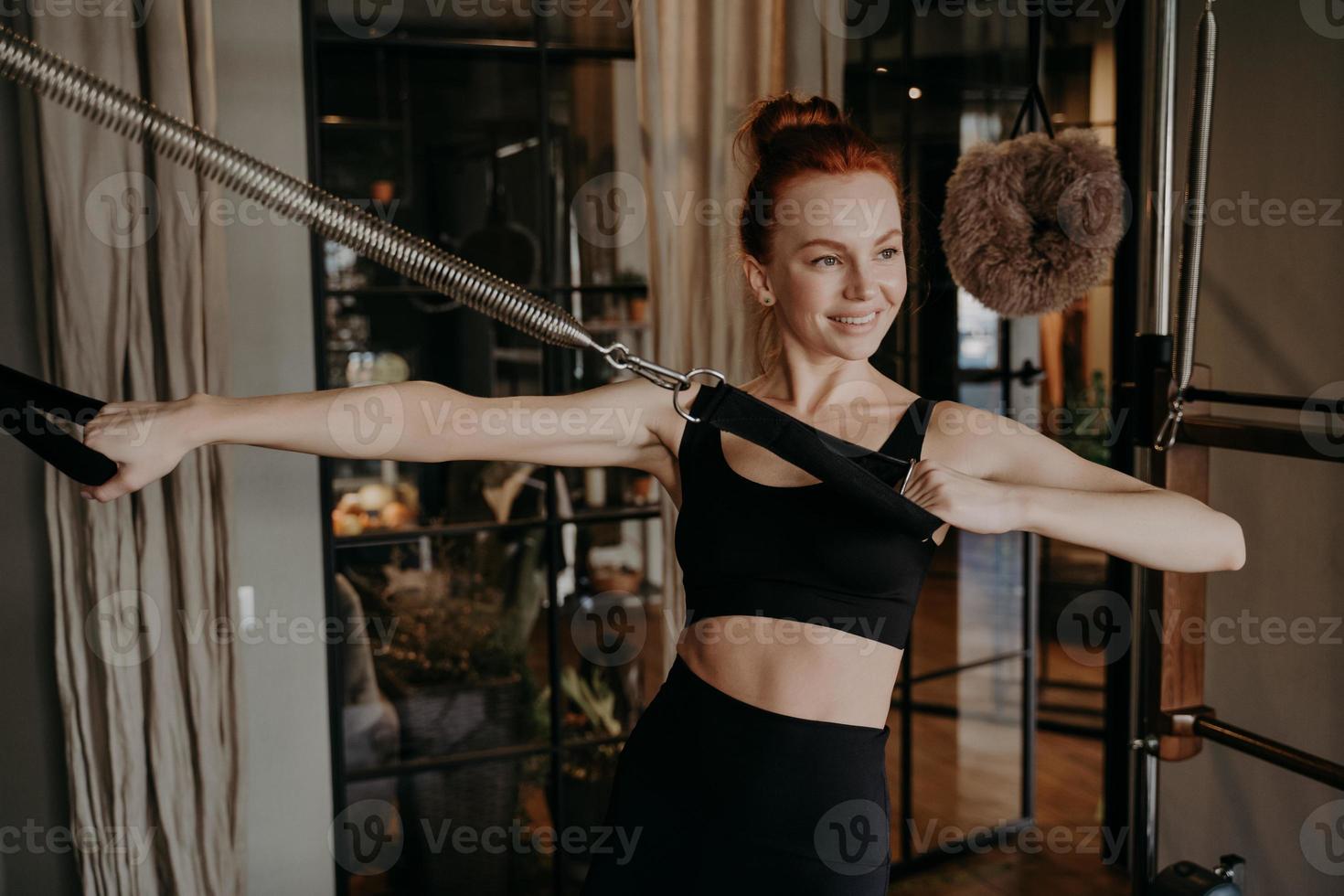 glad ung kvinna pilates instruktör gör hand styrka övning på reformer foto