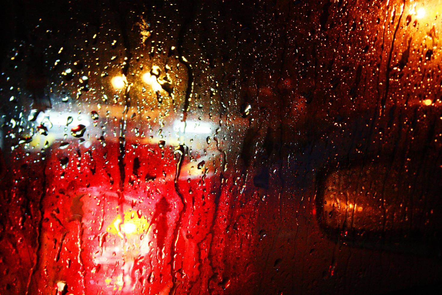 regndroppar konsistens på fönsterglas med gatubelysning abstrakt suddig stadsbild. mjukt fokus foto