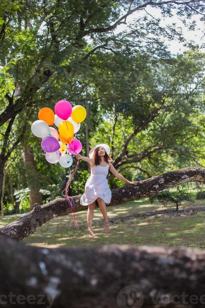 ung tonåring flicka sitter på träd och håller ballonger i handen foto