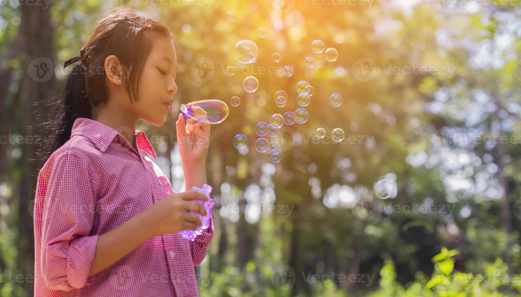 söt liten flicka som bär en rosa skjorta som blåser bubblor i parken, vintage stil. foto