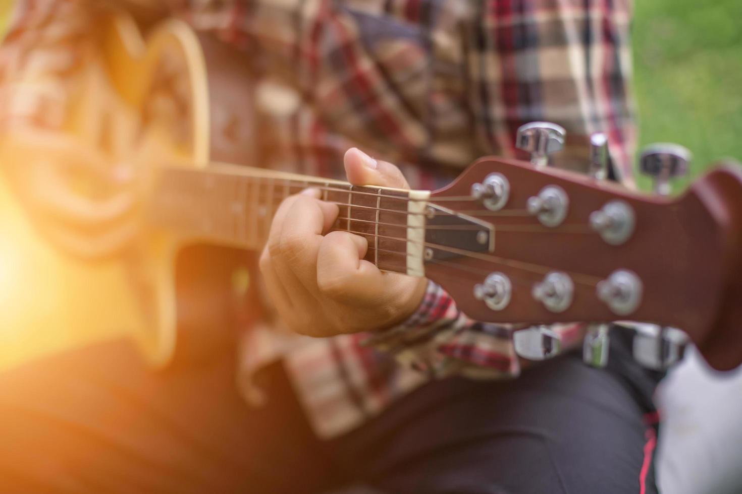 ung hipster man spelar gitarr för att koppla av på sin semester, njuta med naturlig och frisk luft. foto