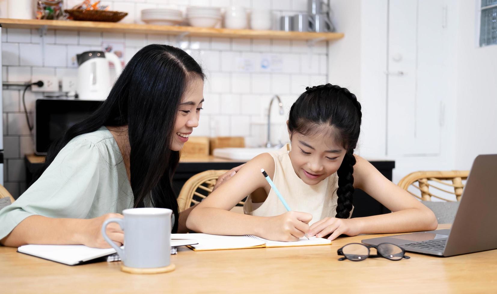 mor och asiatisk unge liten flicka lärande på bärbar dator gör läxor studera kunskap med online utbildning e-lärande system. barn videokonferens med lärare handledare hemma foto