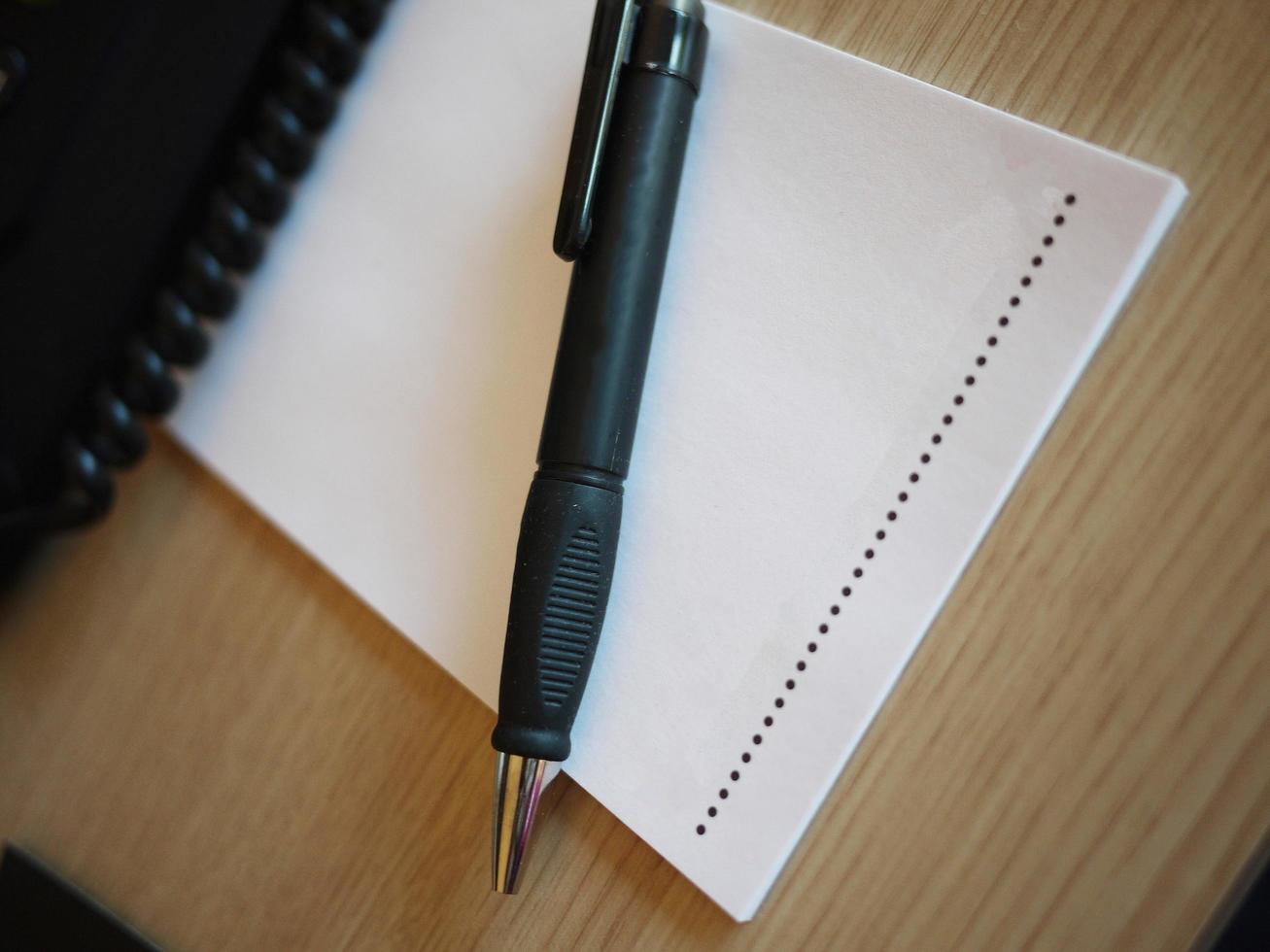 anteckningsblock med svart penna på träbordet och telefonkabel foto