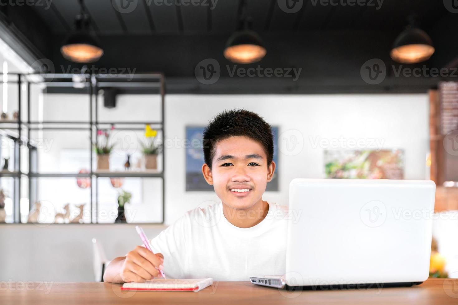 asiatisk glad pojkestudent bär hörlurar och studerar online med videosamtal undervisad av lärare med smart surfplatta och bärbar dator hemifrån under covid-19 foto