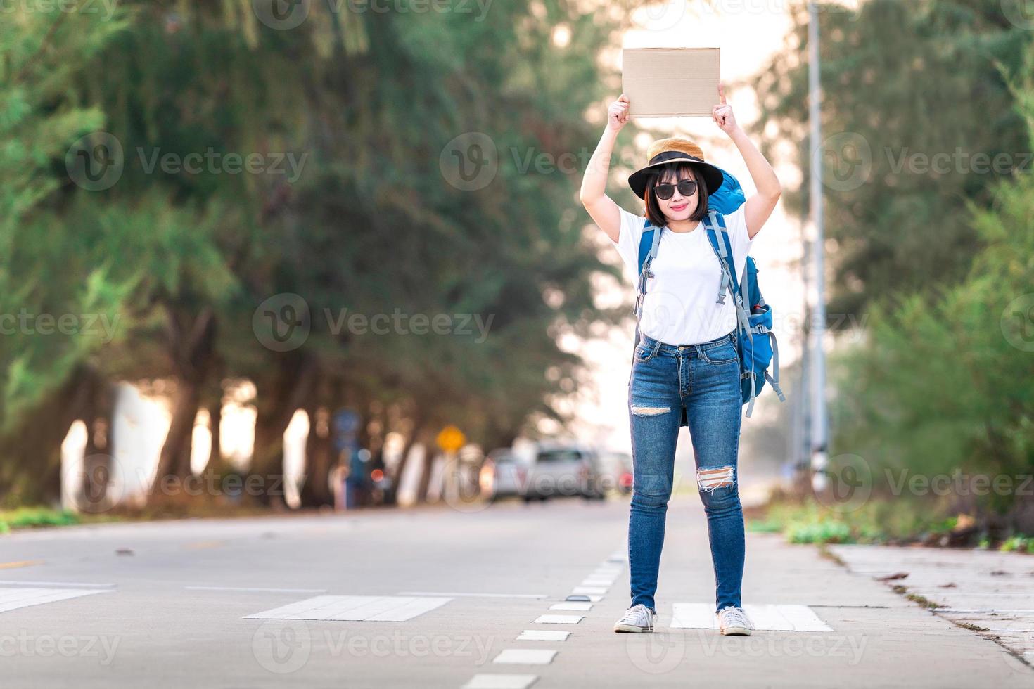 lyckligt leende liftare asiatisk kvinna ryggsäck väntar på biltransport under helgen för resor och resa resa i semester vid solnedgången foto