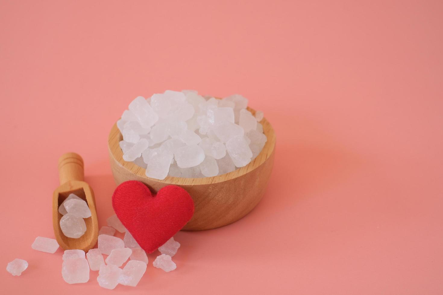 vitt candy rock socker, kristallsocker i träskopa och glasburk med rött hjärta på rosa bakgrund. valt fokus. utrymme för text. foto