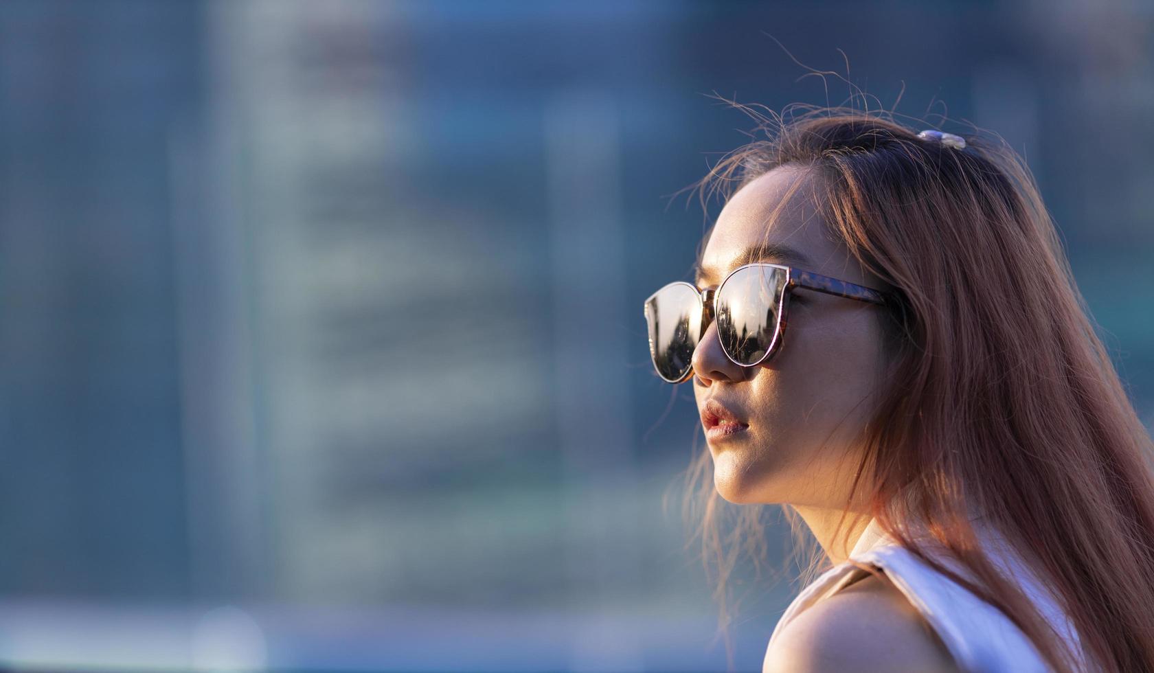 asiatisk kvinna modell med ingefära hår bär solglasögon medan du tittar direkt mot solen med kopia utrymme foto