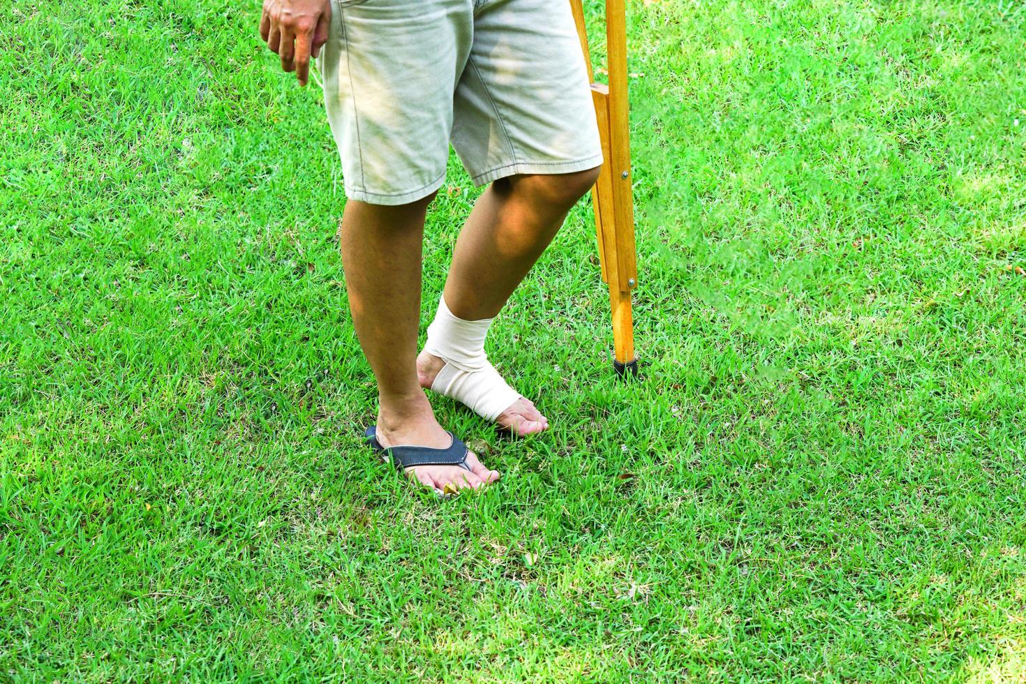 bilden visar patienter med fotledsskador med bandage fotledsstöd och använda kryckor för att stödja gång på gräsmattan. hälsovård och medicinsk koncept. foto