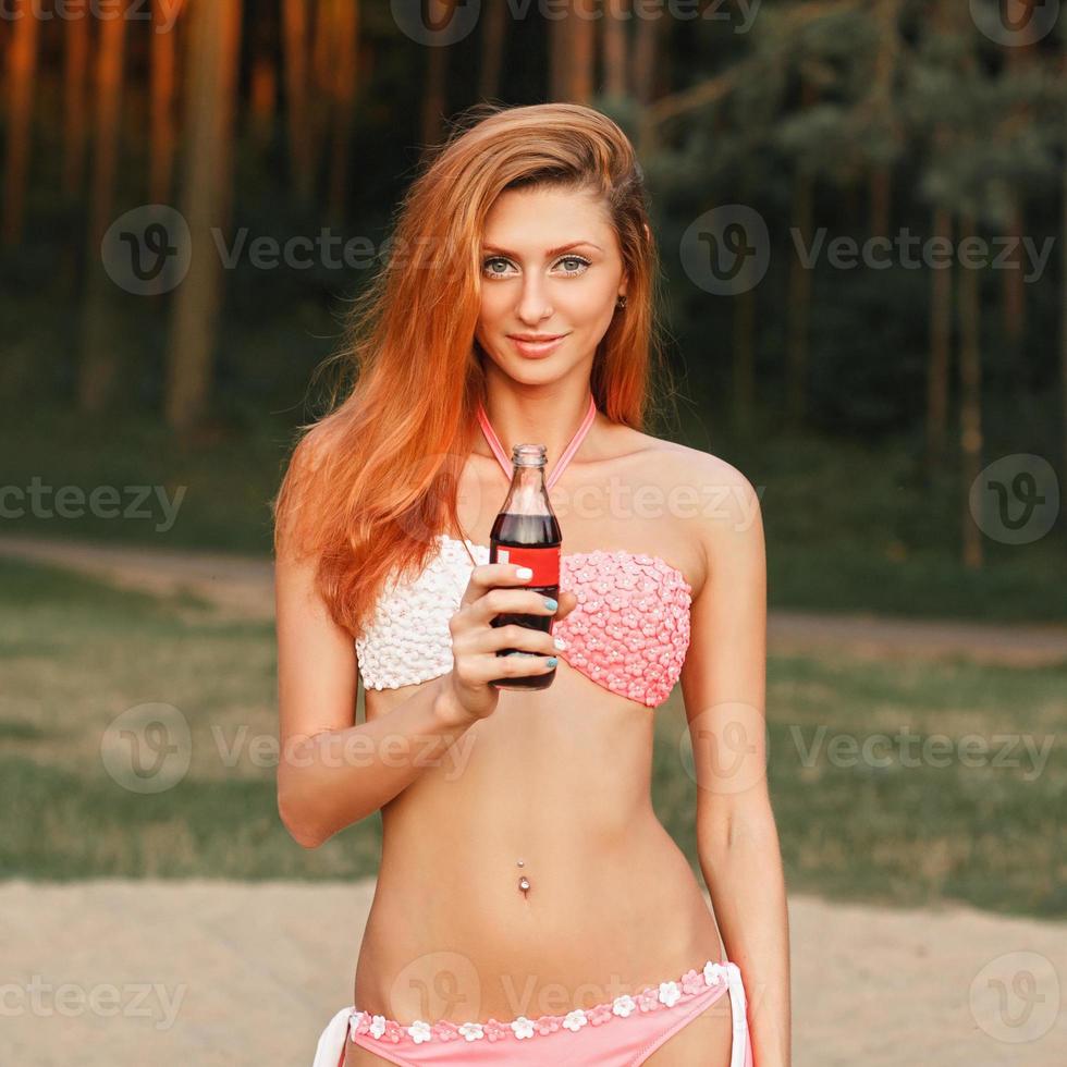 vacker flicka med rött hår som håller en flaska drink foto