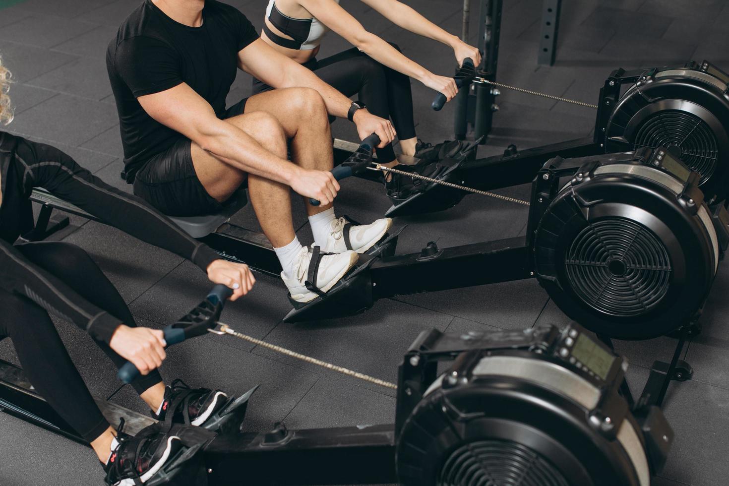 ung man och vackra kvinnor tränar med roddmaskin på crossfit gym. foto