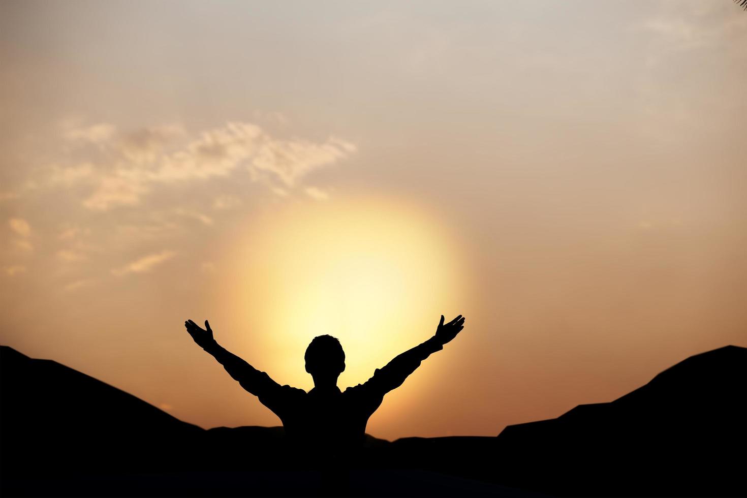 siluett av en man lyfter upp händerna och dyrkar gud vid solnedgången. begreppet religion. foto