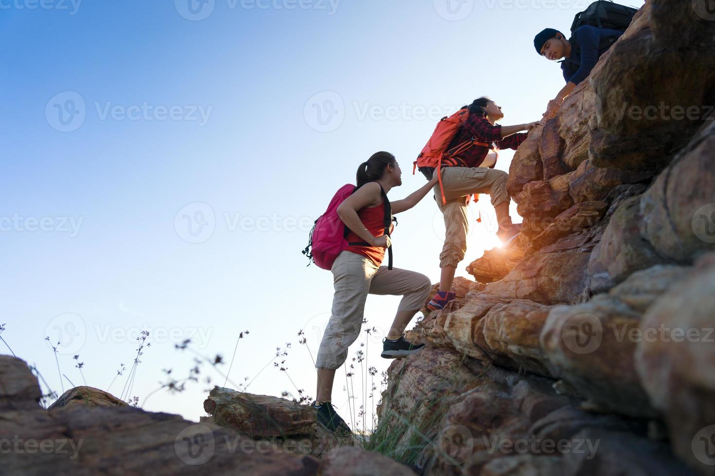 ungt asiatiskt par klättrar upp på berget, vandring och lagarbete koncept. foto
