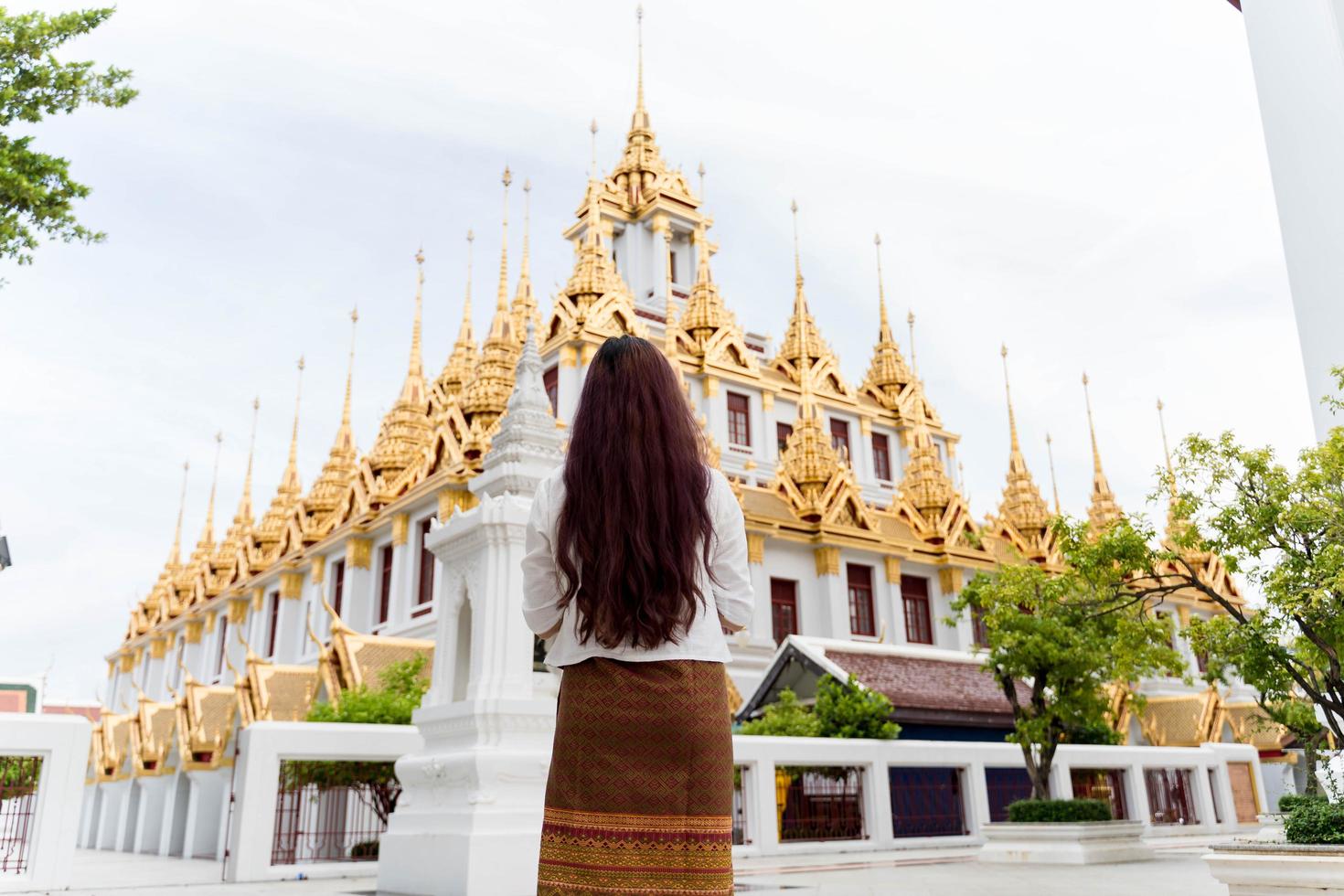 ung asiatisk kvinna klädd i traditionell klänning i thailand ber på wat ratchanatdaram foto