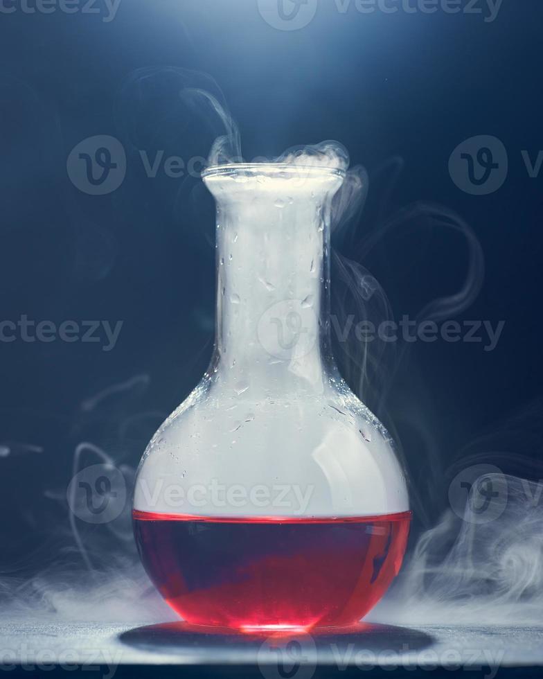 glaskolv med en röd vätska ryker på en grå bakgrund. foto