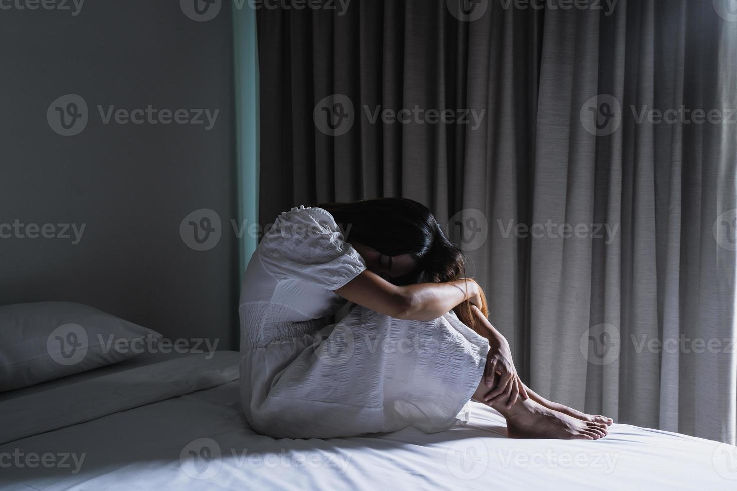 ensam ung kvinna känner sig deprimerad och stressad sittande i det mörka sovrummet, negativa känslor och mental hälsa koncept foto