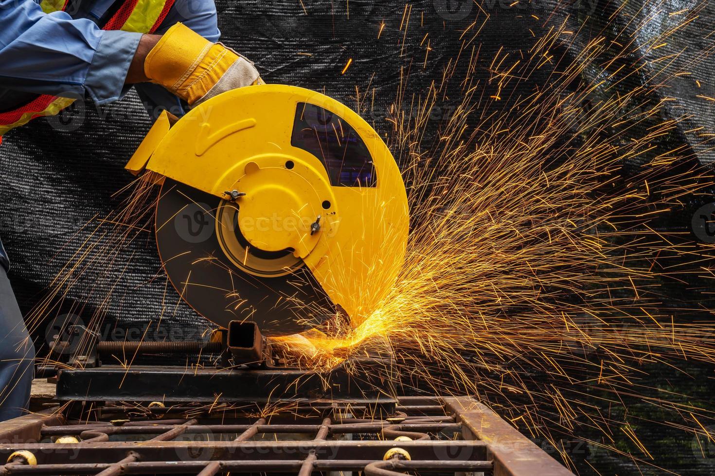 industritekniker ingenjör i blå skyddsduk bär säkerhetsmask, man som arbetar med elektrisk slipverktyg på stålkonstruktion med gnistor flygande i fabriken, selektivt fokus foto