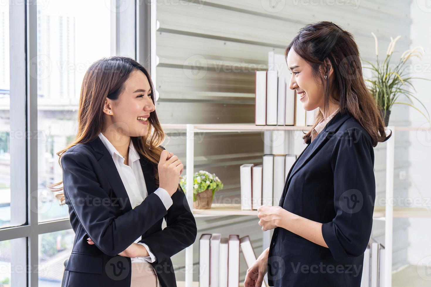 leende två affärskvinna som pratar med partner medan de står i modern kontorsinredning, team av professionella anställda diskuterar idéer om projekt efter mötet foto