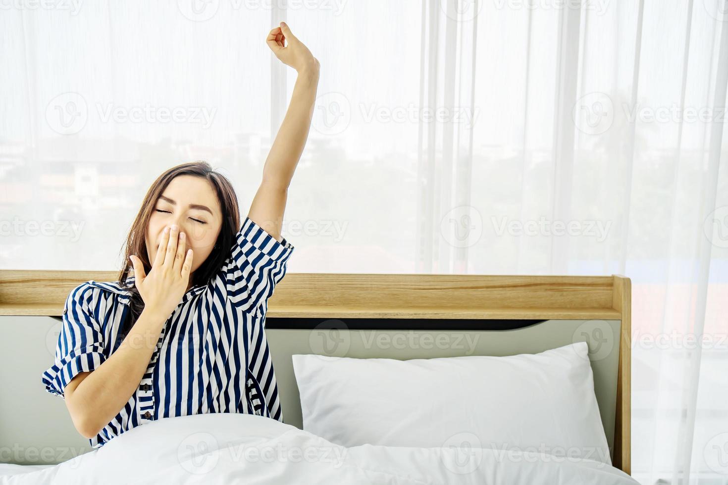 vila, semester, komfort och folkkoncept, porträtt av sömnig asiatisk kvinna i sovkläder som gäspar efter att hon vaknat så tidigt på morgonen, sittande i sängen foto