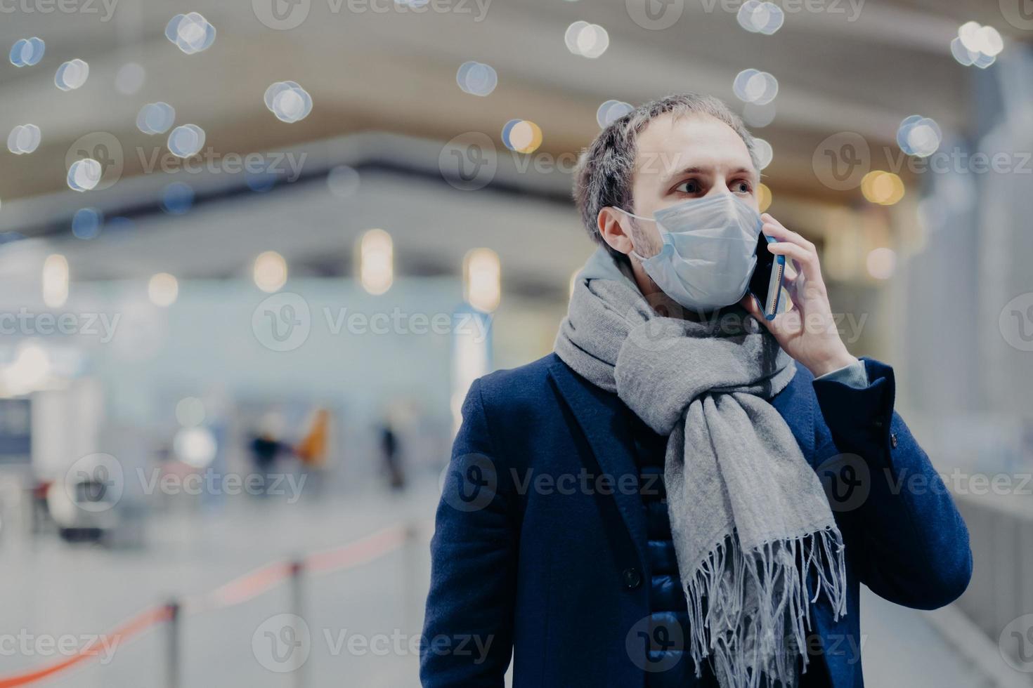 hälsa, kommunikation och epidemi koncept. seriös man bär skyddande medicinsk mask, bryr sig om säkerheten för att inte fånga coronavirus, går i köpcentrum, pratar via mobiltelefon. antivirusskydd foto