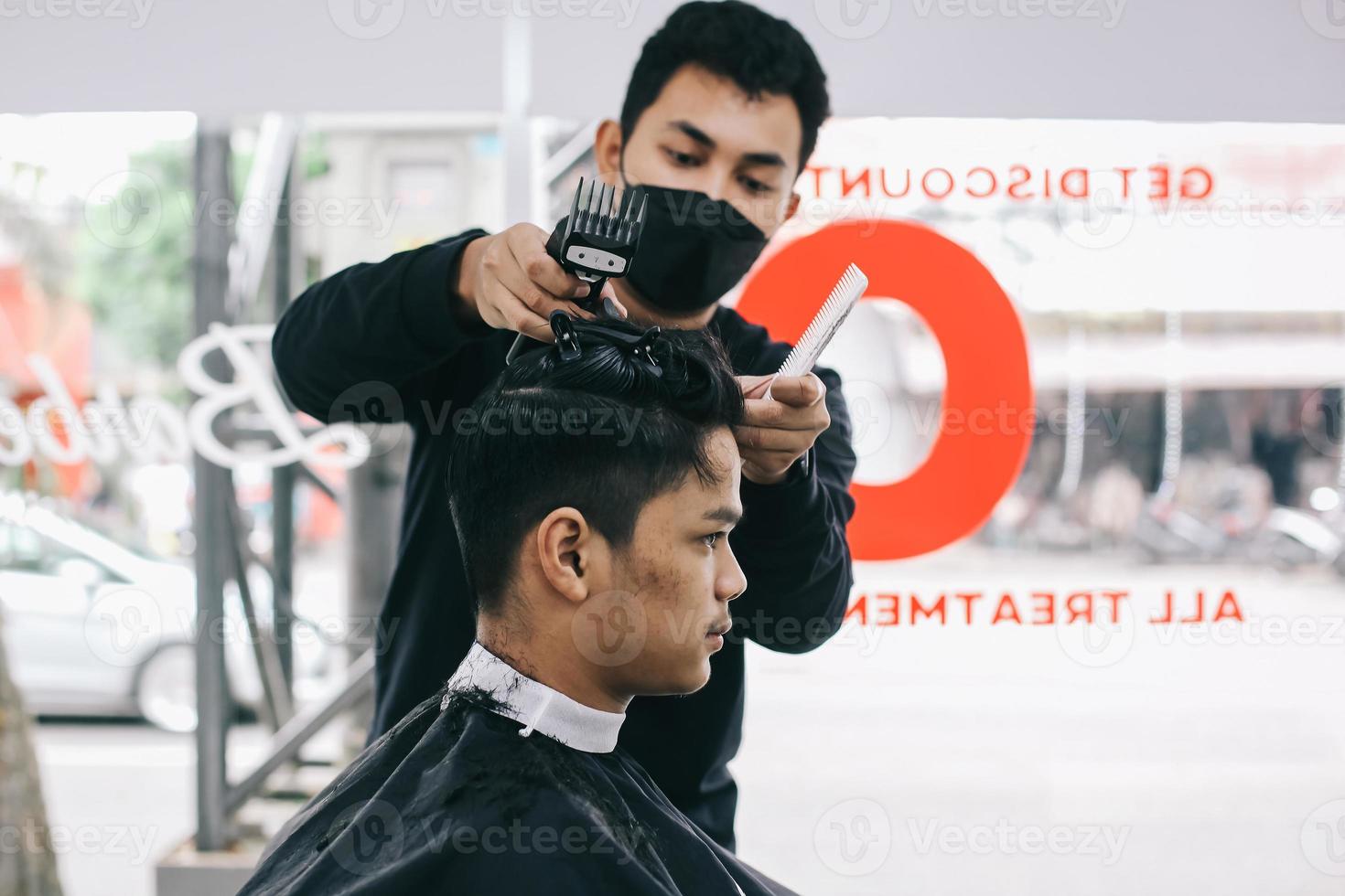 självsäker man besöker frisören på frisörsalongen. frisör som rakar sin klients hår med klippmaskin i salongen. självvård, maskulin skönhet. barberare. foto