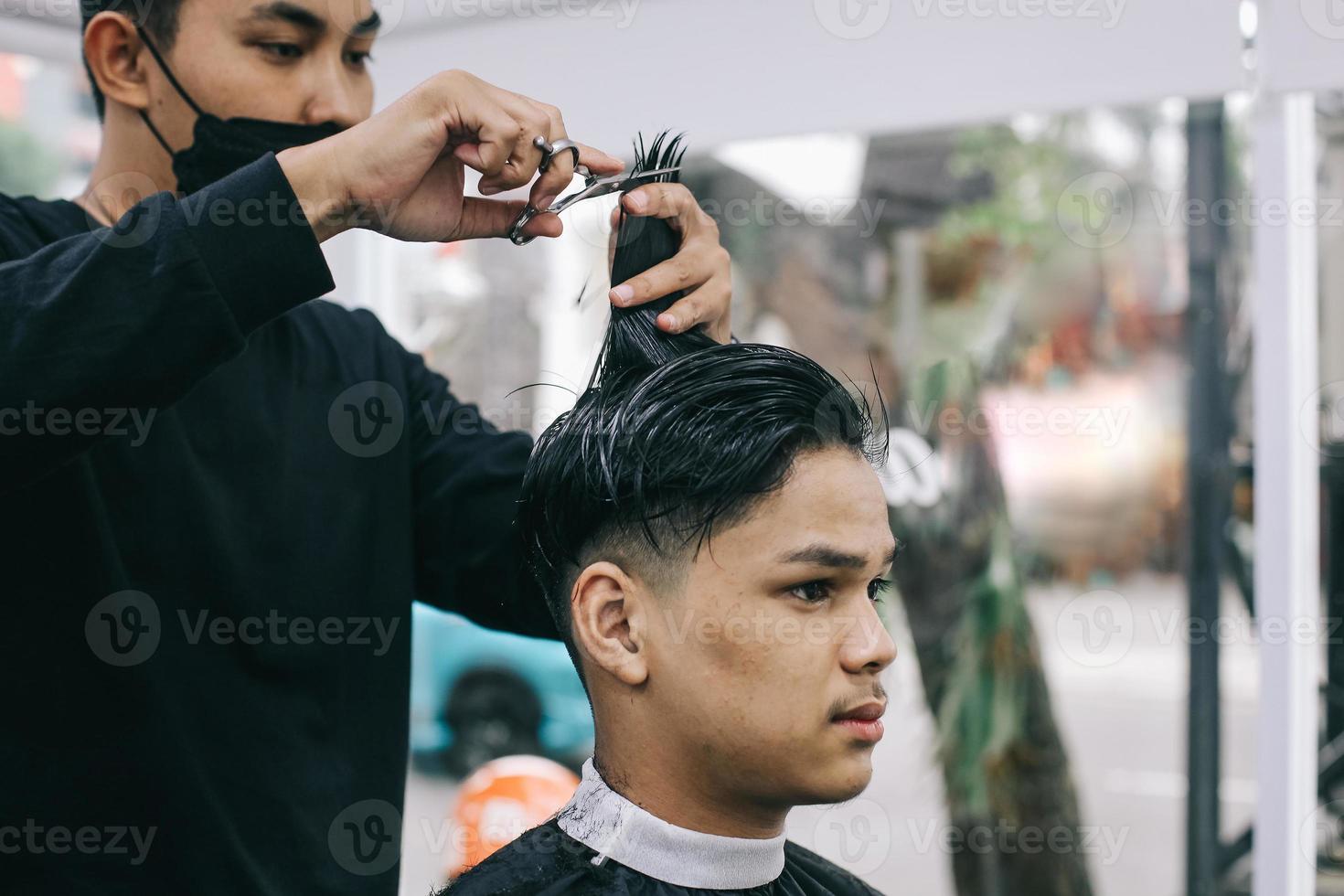 ung man besöker barbershop. frisören rakar konsumentens hår i salongen. egenvård, maskulin skönhet. barberare. foto