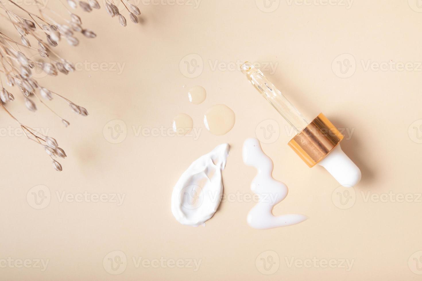 pipett och kosmetiska utstryk med kräm och droppar olja eller serum på en beige bakgrund ovanifrån foto