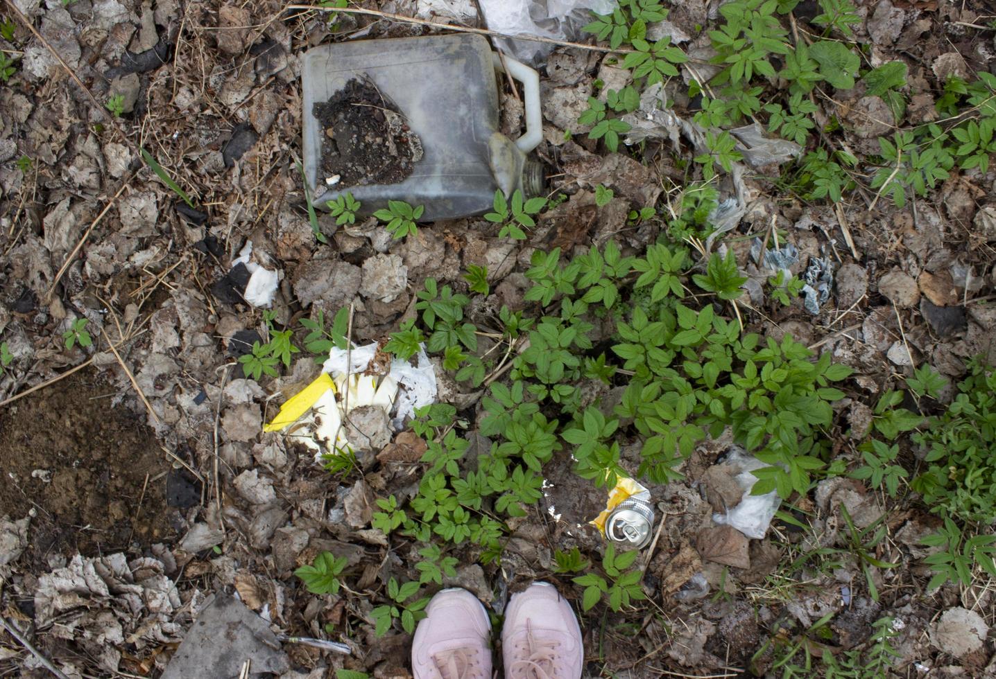 fötter som står på marken med torra löv, grönt gräs och sopor. miljöföroreningar koncept. skräp under fötterna foto