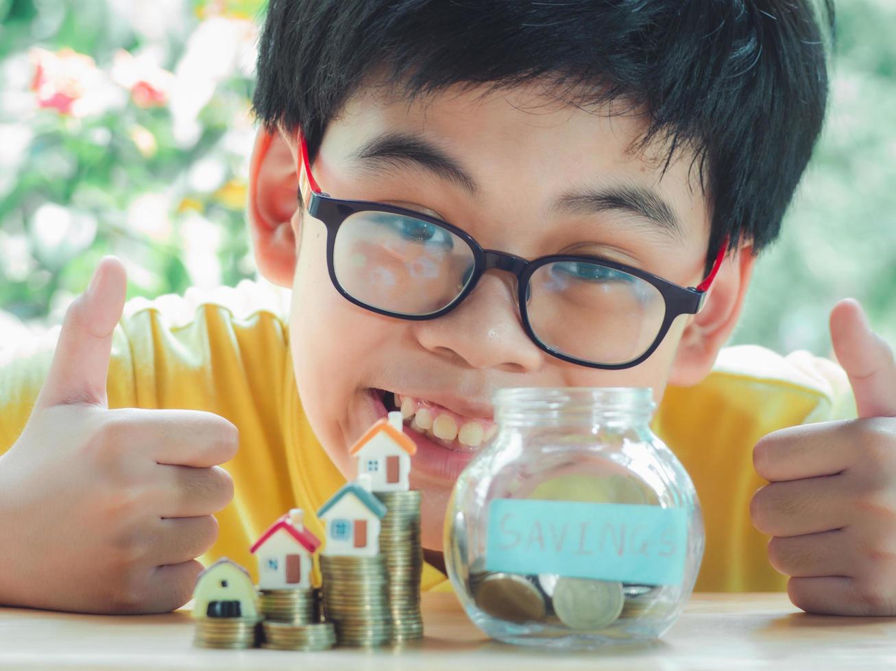 asiatisk pojke som håller mynt släpp en behållare spara pengar för att spara pengar investera för framtiden och köpa home.concept lån, egendom stege, finansiella, fastighetsinvesteringar och bonus. foto