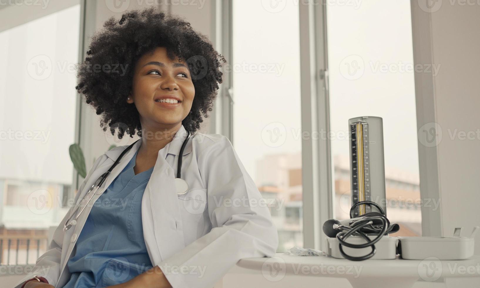 porträtt av en leende kvinnlig läkare som bär en vit rock med ett stetoskop på ett sjukhuskontor. foto