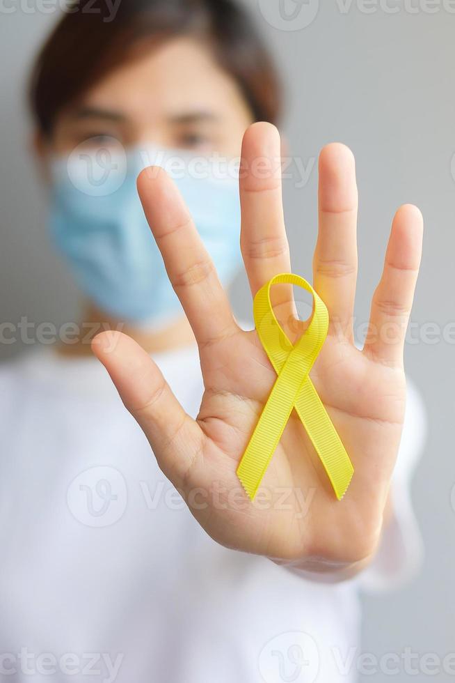 hand som håller gult band för att stödja människor som lever och sjukdom. September självmordsförebyggande dag, barndom, sarkom och bencancer medvetenhet månad koncept foto