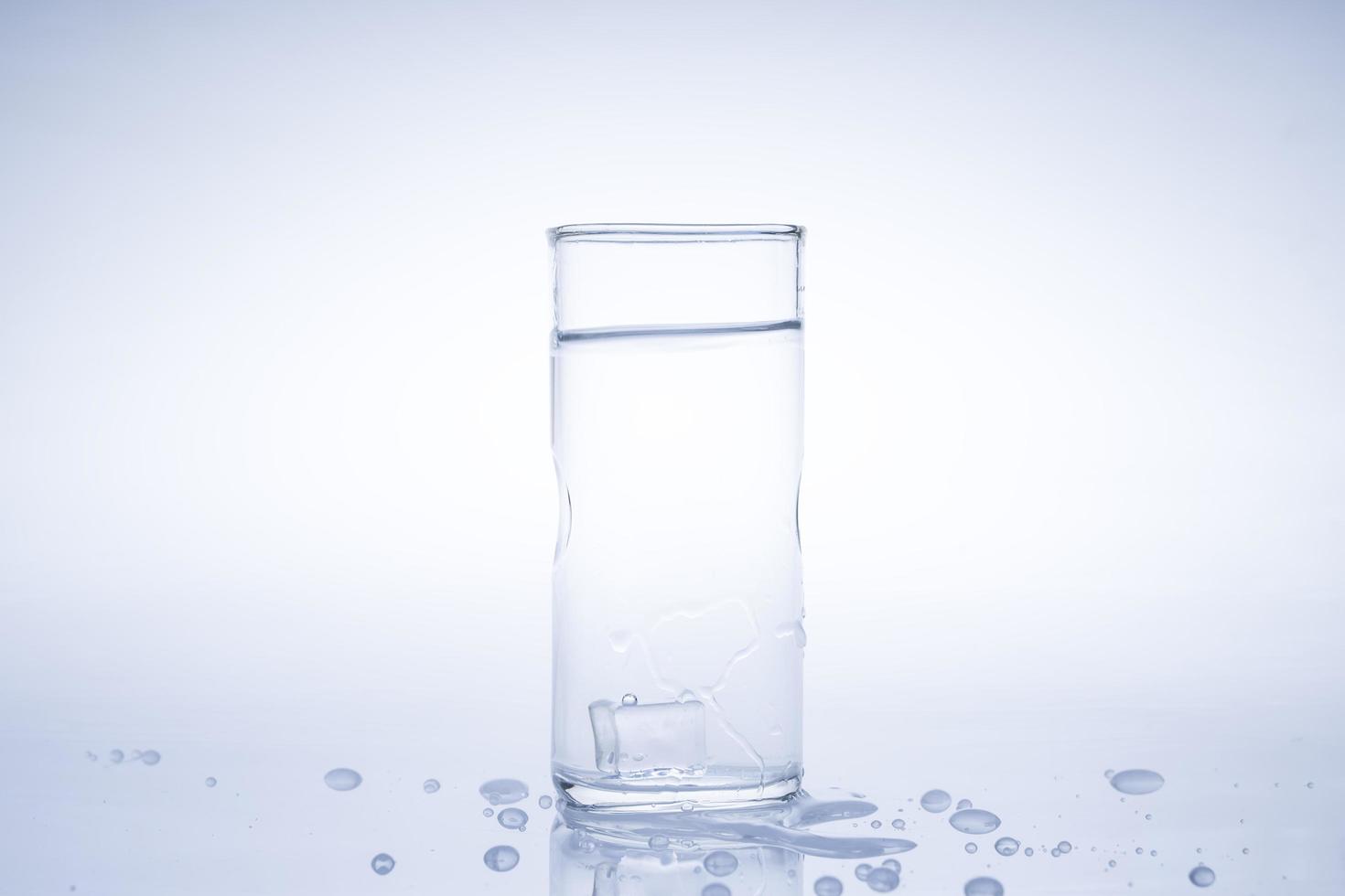 isbit föll i glaset med vatten. vatten stänkte från det klara glaset. färskt koncept foto